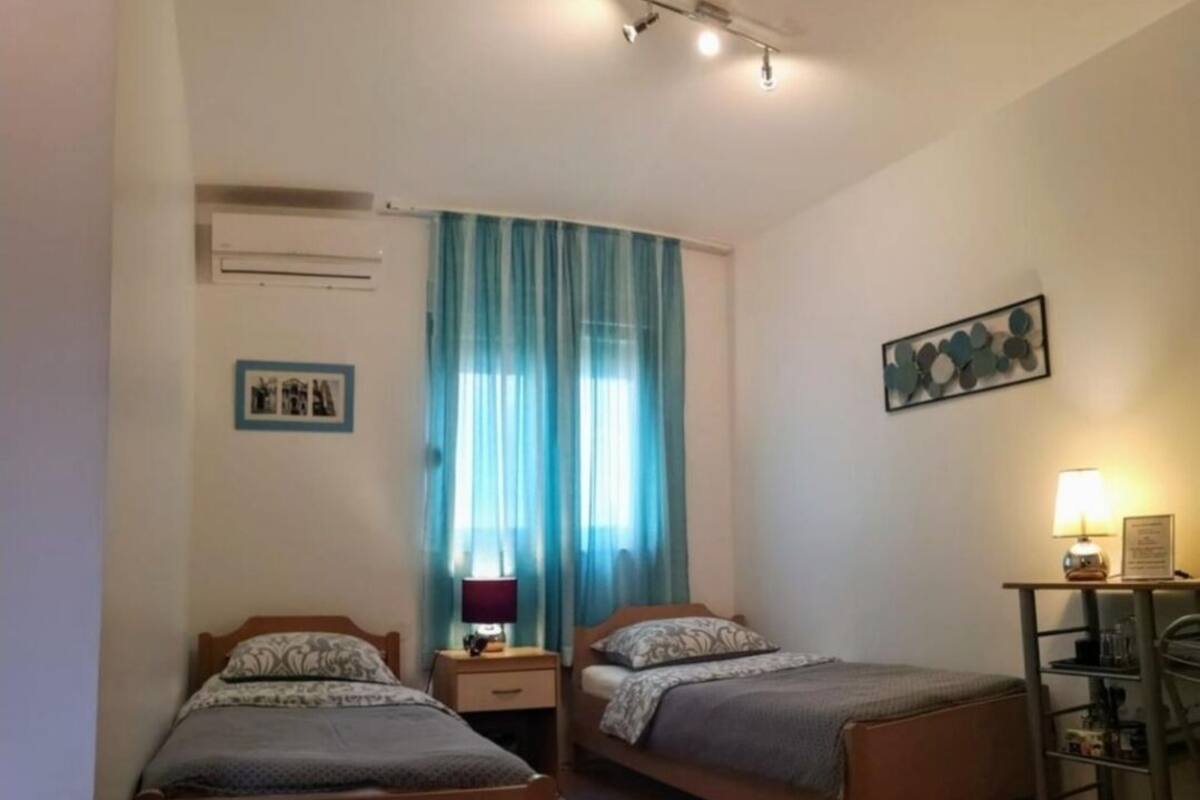 A bedroom with two beds, a desk, a chair, a lamp, and a picture on the wall.