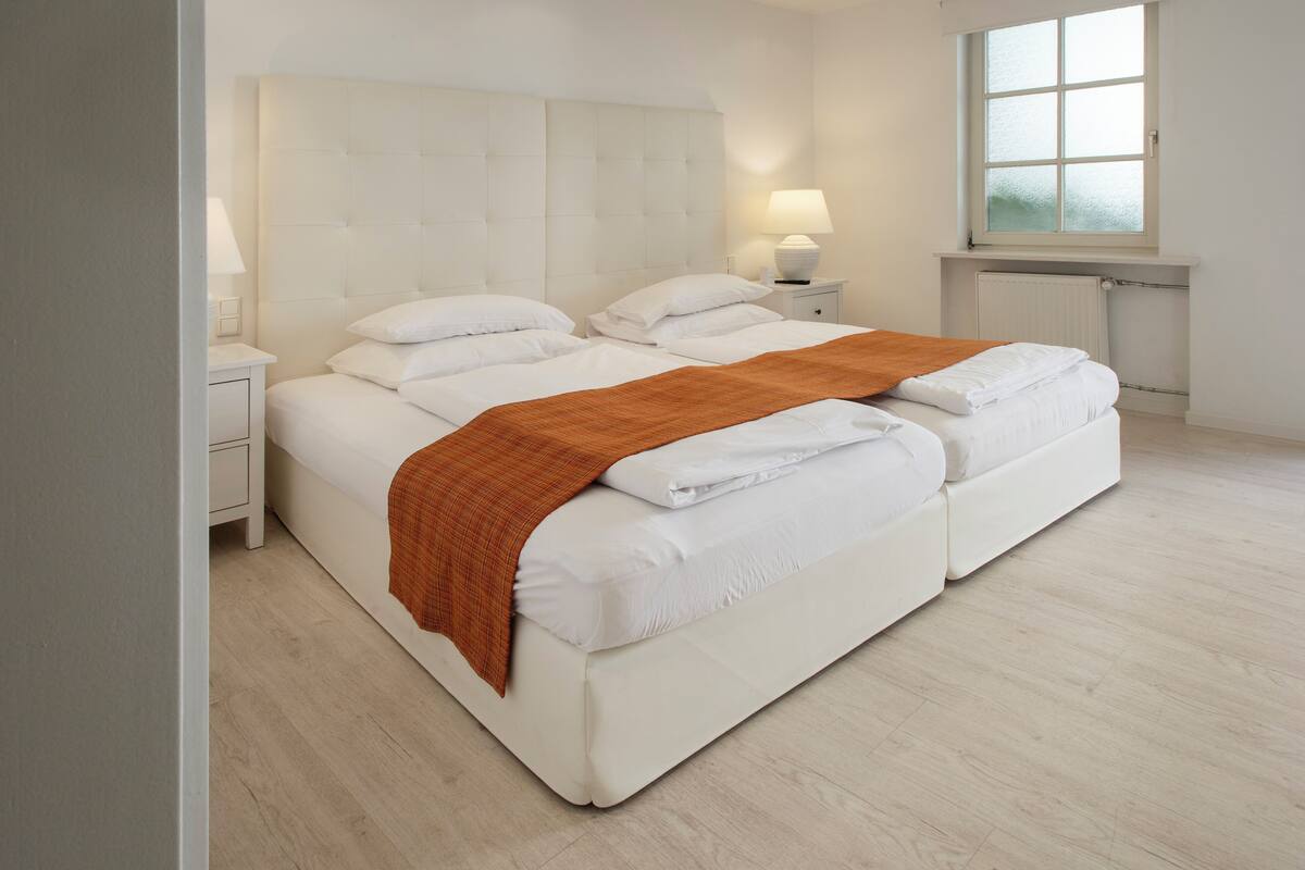 A double bed with a white headboard and two bedside tables, one with a lamp.