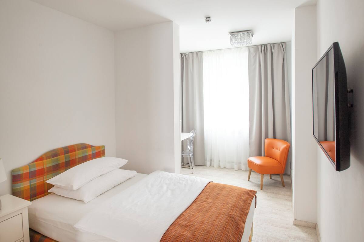 A hotel room with a bed, a chair, a TV, and a window with curtains.