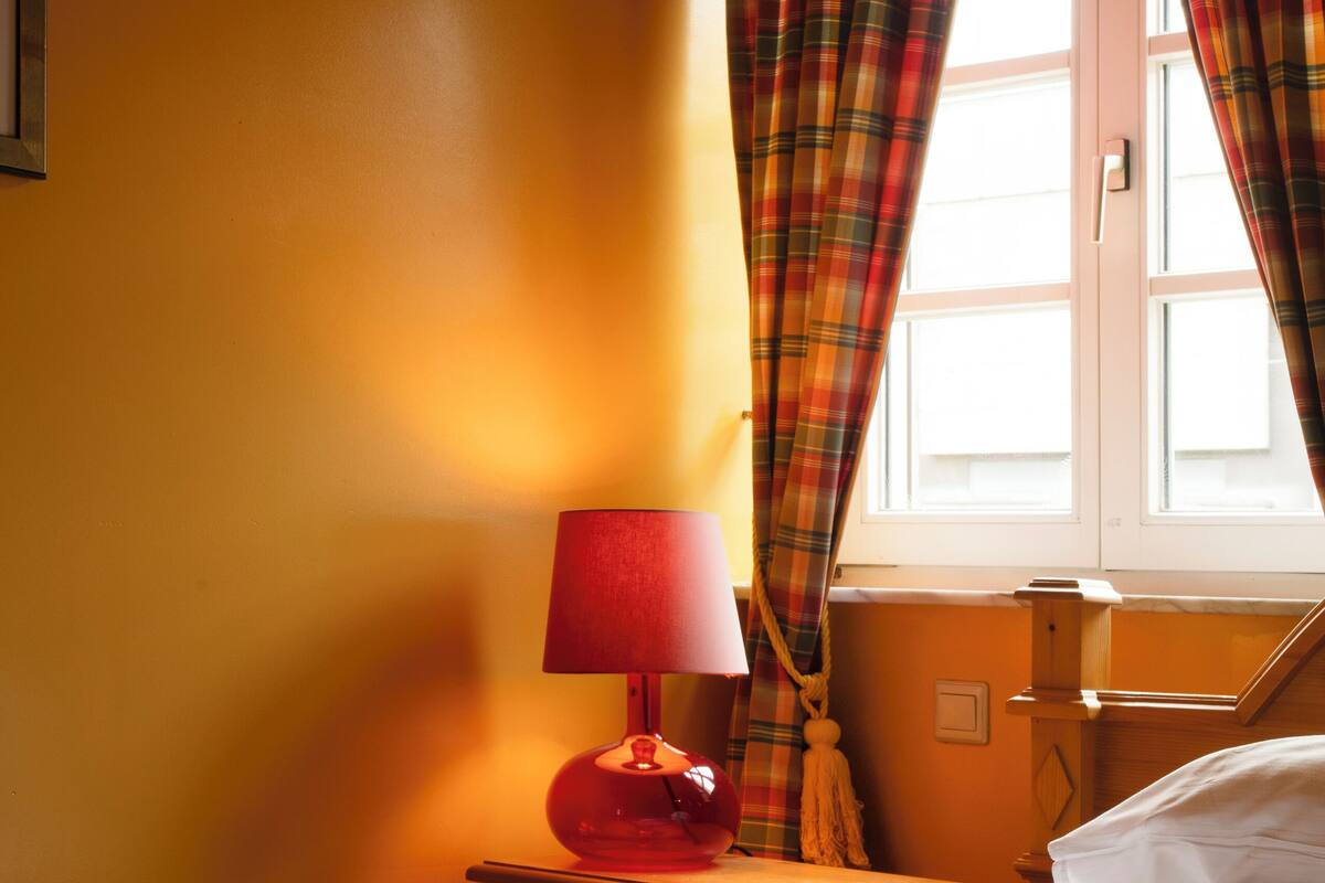 A hotel room with a bed, a nightstand with a lamp, and a window with curtains.