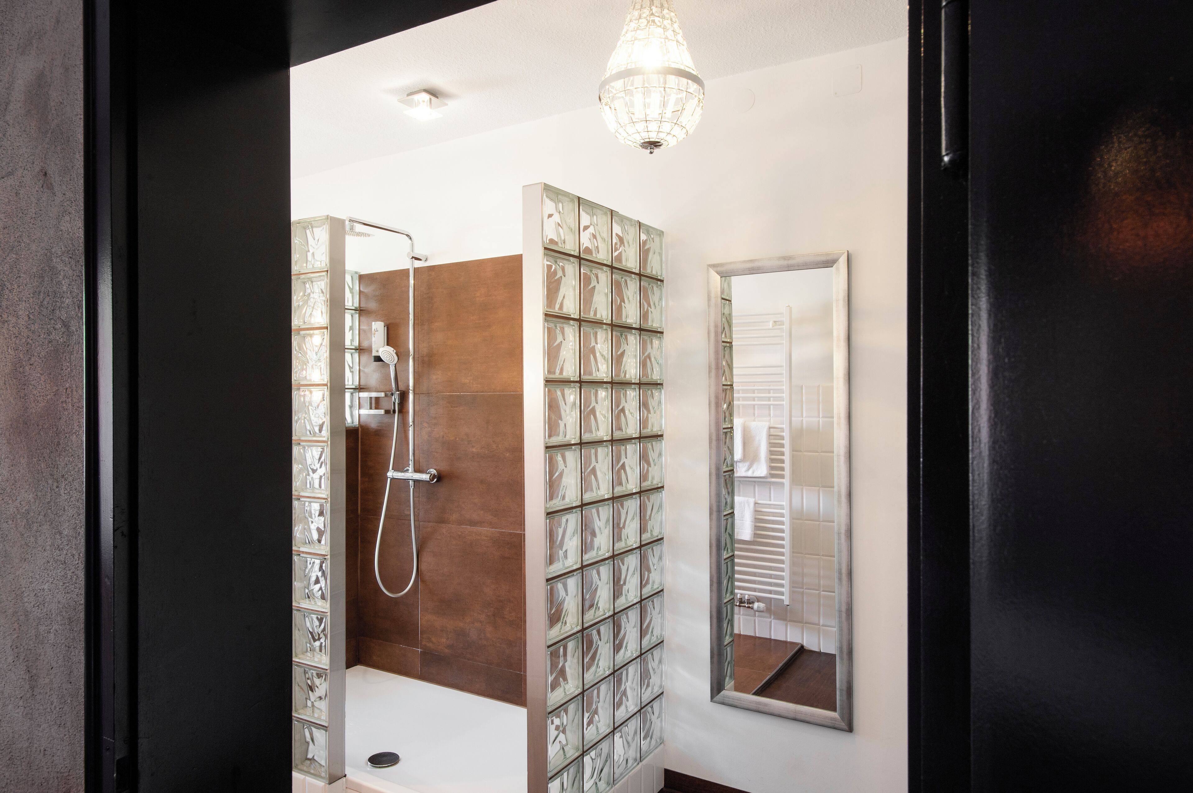 A modern bathroom with a glass shower enclosure, a large mirror, and a decorative light fixture.