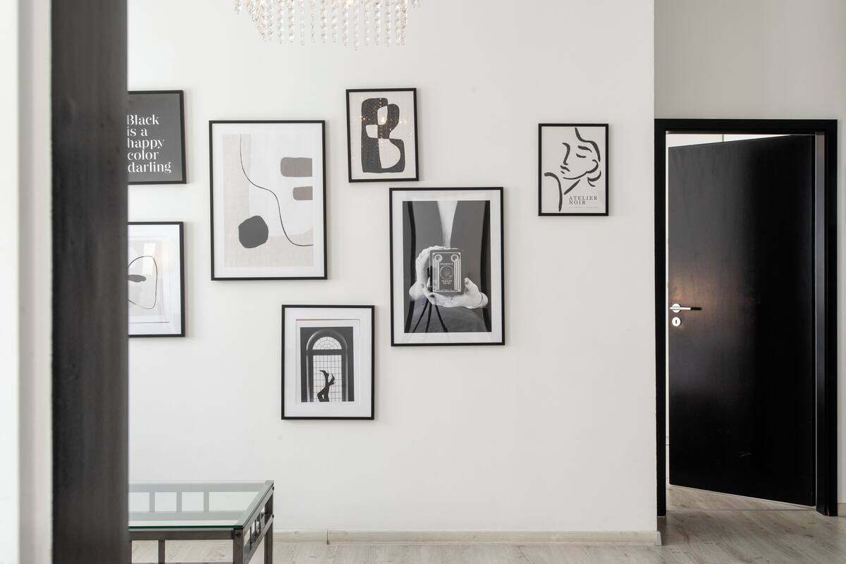 A hallway with a series of framed artworks on the wall, a bench, and a door.