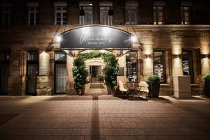 La entrada del Hotel Wenders Boutique, con un cartel sobre la puerta, fachada de ladrillo y una pequeña zona de estar al aire libre con sillas y mesas.