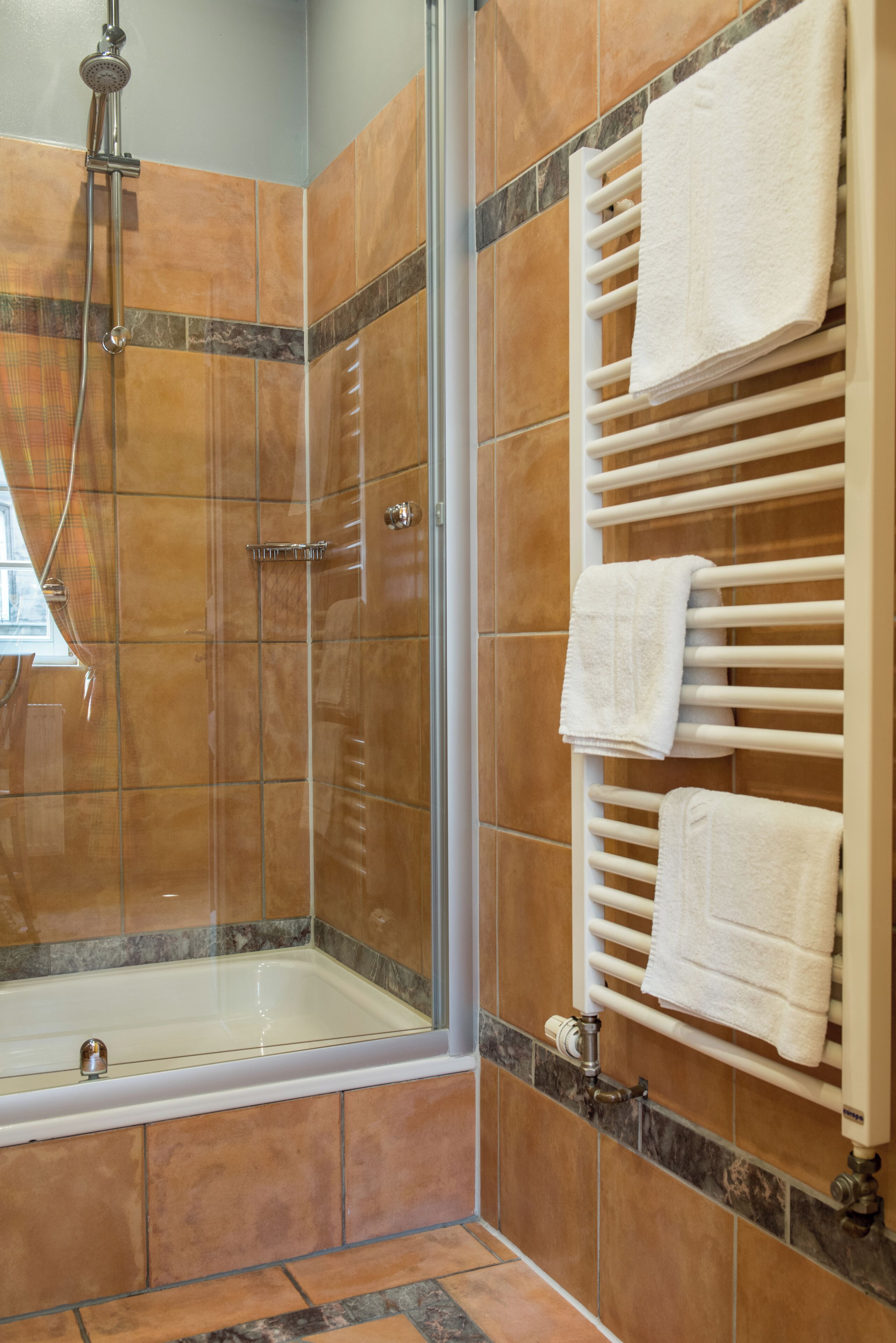 Ducha con puerta de vidrio, toallero blanco con toallas y bañera.