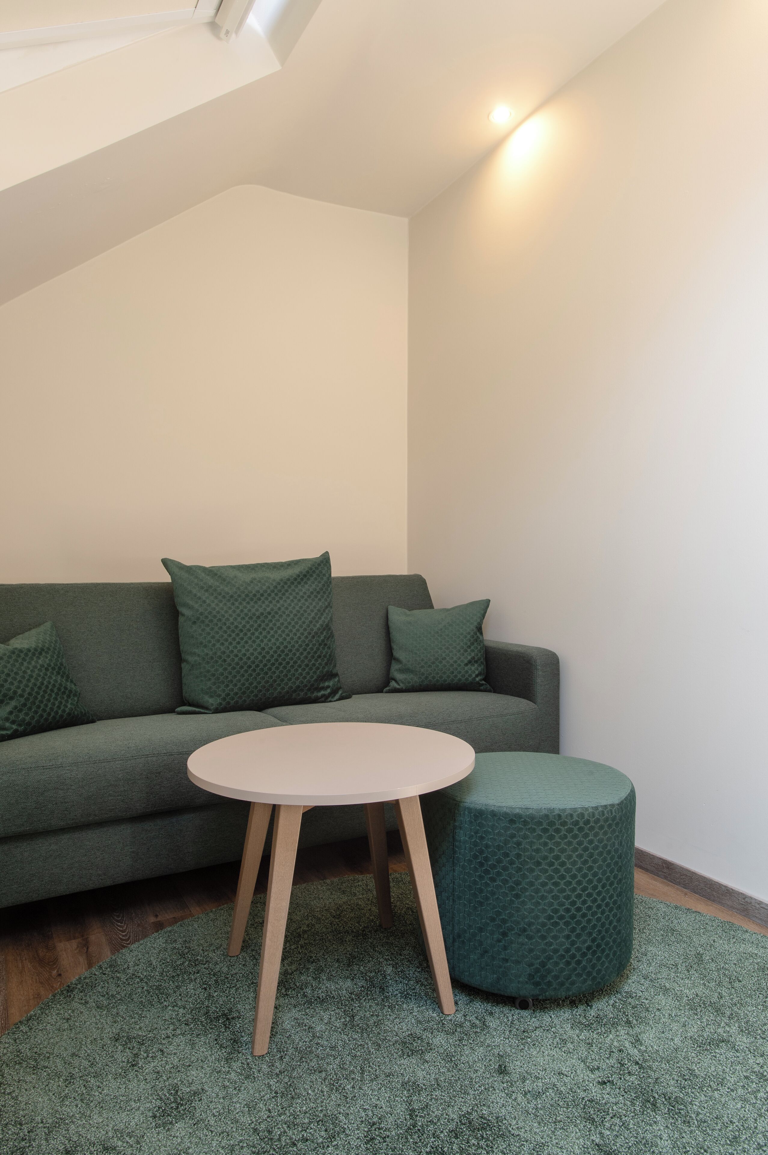 Una sala moderna con un sofá verde, una mesa redonda y un otoman a juego.