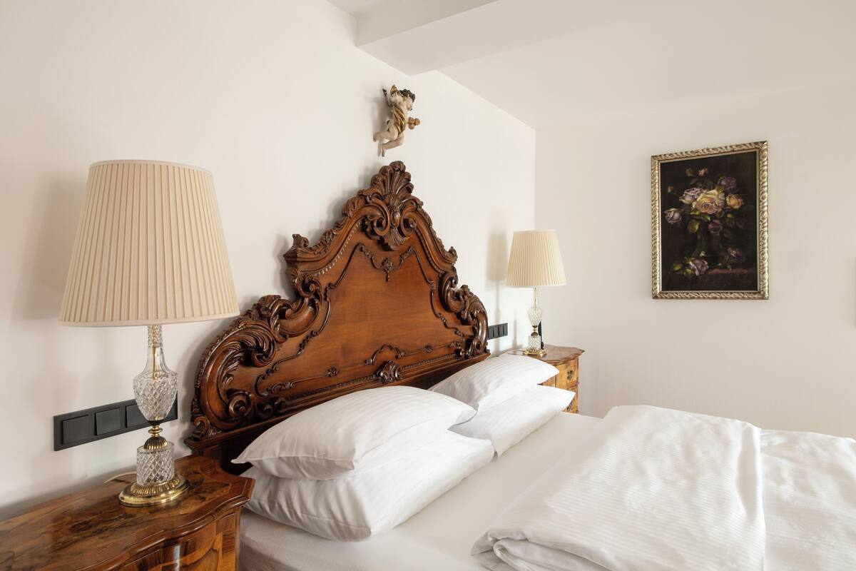 A neatly made bed with white linens, a wooden headboard with intricate carvings, and two bedside lamps.