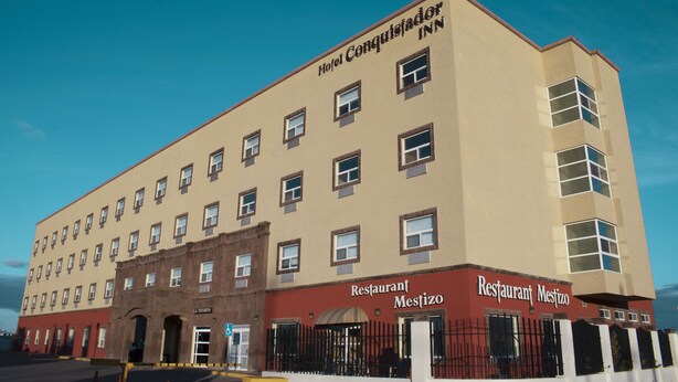 Un hotel con varios pisos, un restaurante en la planta baja llamado 'Restaurant Mestizo', y un letrero que dice 'Hotel Conquistador INN'.