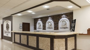 Un mostrador de recepción de hotel con tres relojes etiquetados 'Camino Real', 'Camino Real' y 'Los Angeles'.
