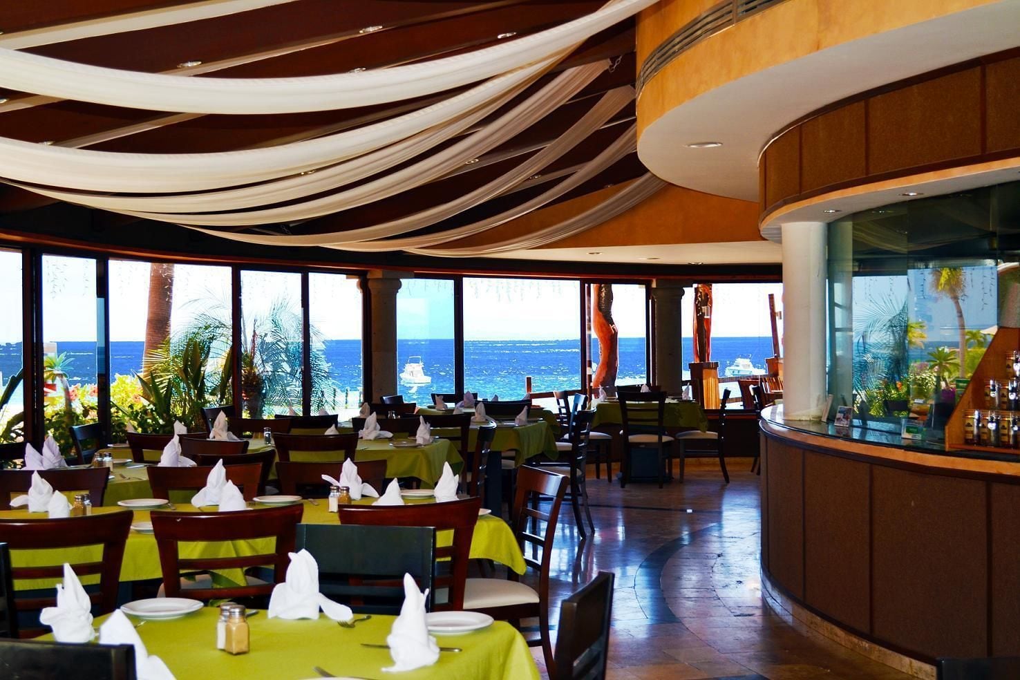 A restaurant with tables set for dining, large windows offering a view of the ocean, and a curved counter area.