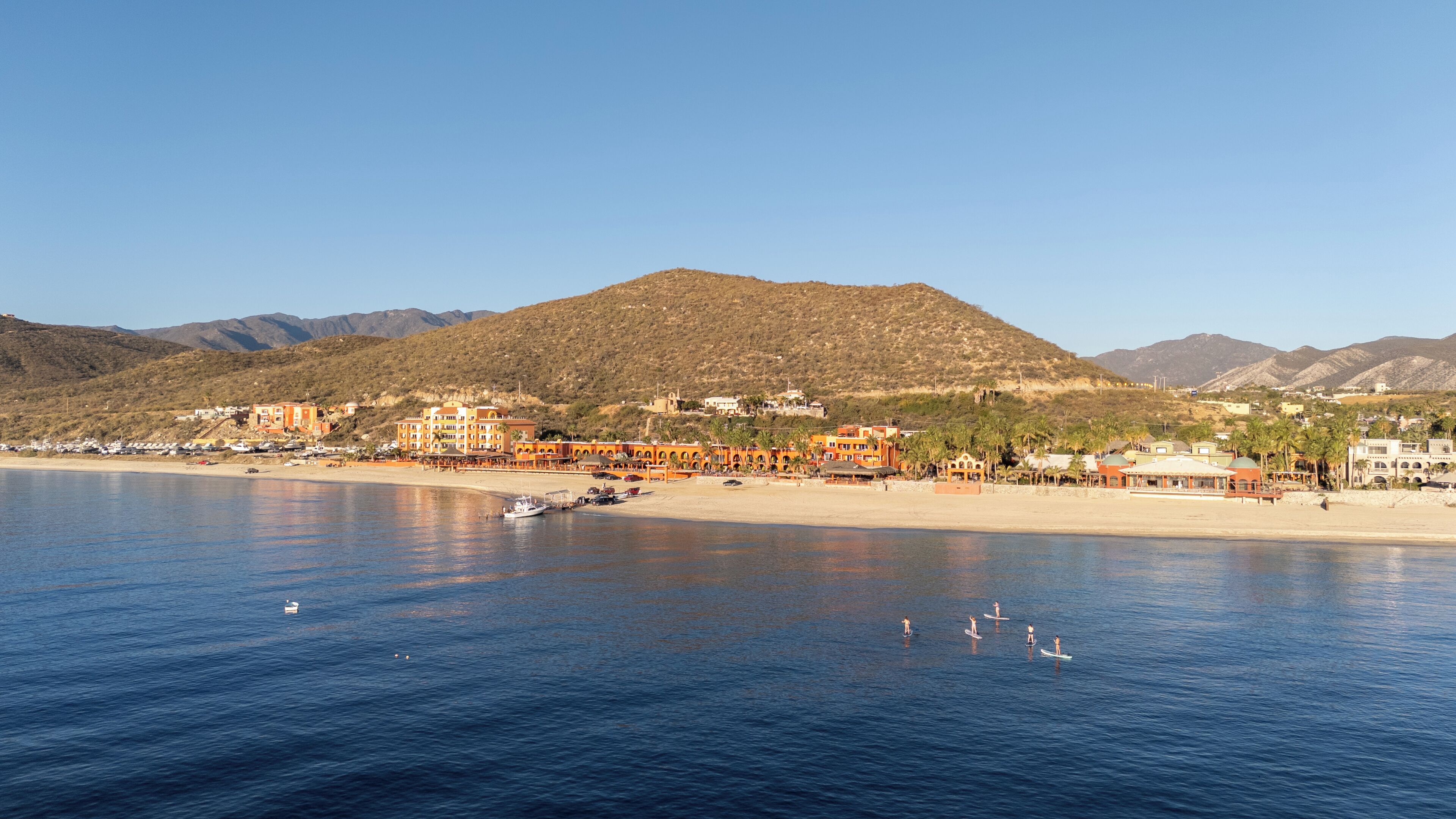 A coastal town with buildings along the beach and a mountain in the background.