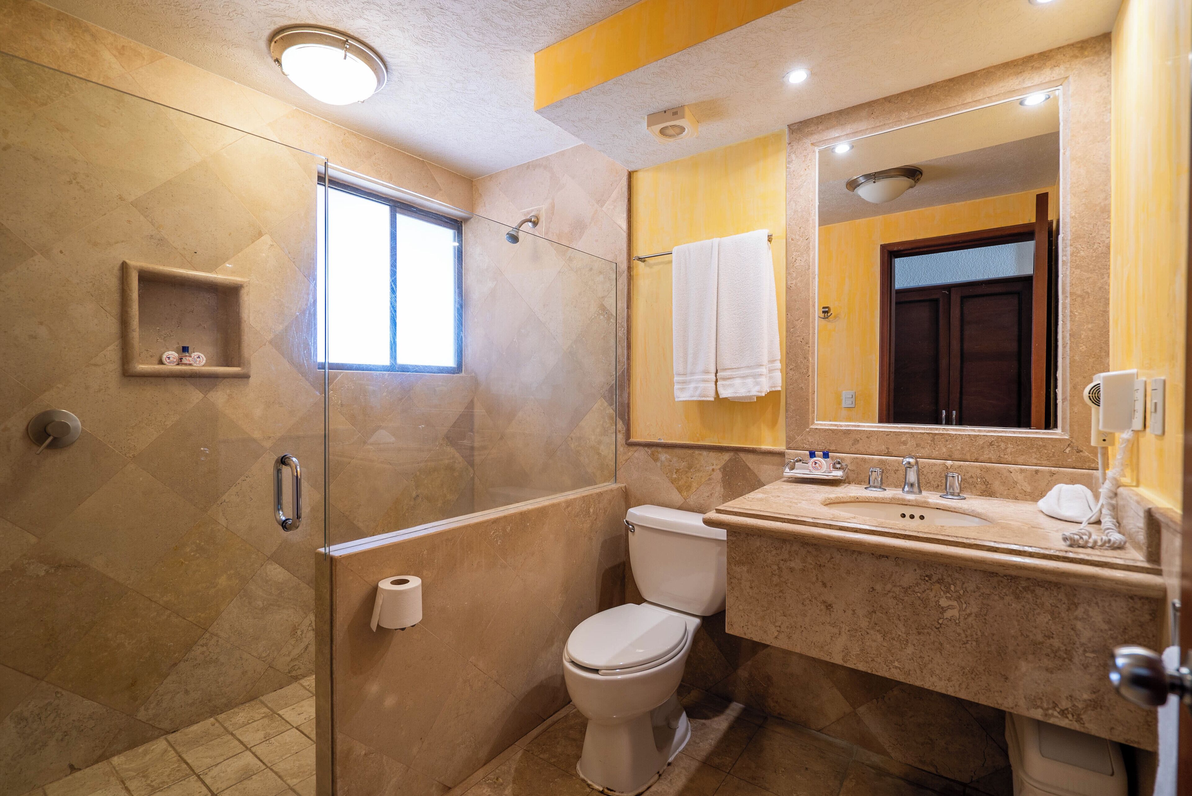 A bathroom with a glass-enclosed shower, a toilet, a sink with a mirror, and a towel rack.