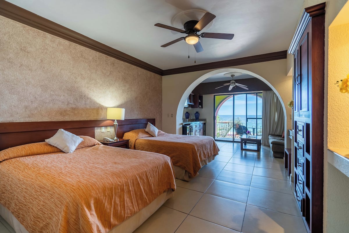 Une chambre d’hôtel avec deux lits, un ventilateur de plafond, un balcon et une vue sur l’océan.