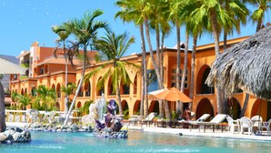 Un resort con piscina, palmeras y un edificio con arcos y techo de paja.