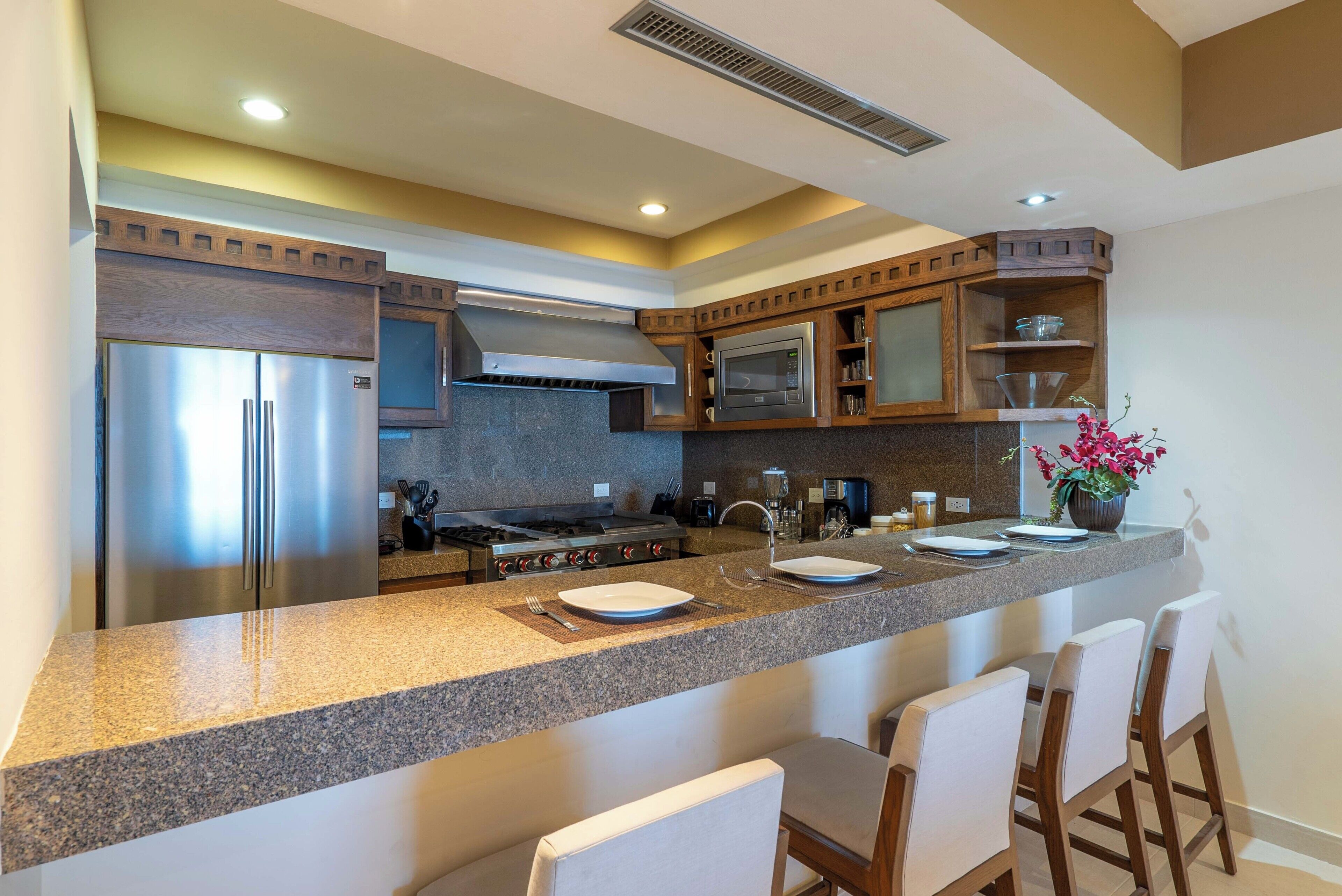 Une cuisine moderne dotée de plans de travail en granit, d’appareils électroménagers en acier inoxydable et de meubles en bois.