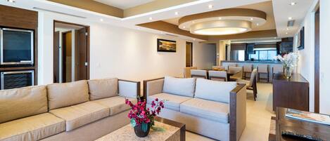 A modern living room with a sectional sofa, a coffee table with a vase of flowers, and a dining area in the background.
