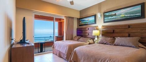 A hotel room with two beds, a ceiling fan, a TV, a painting, and a view of the ocean.