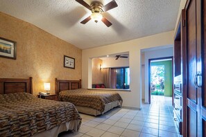 Habitación de hotel con dos camas, un ventilador de techo, una ventana con vistas y una puerta que da a otra habitación.