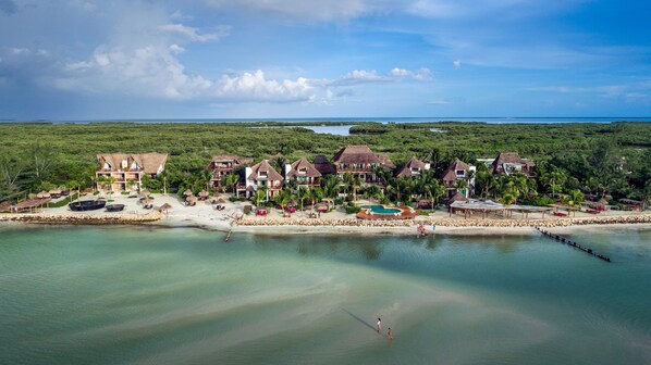 Un resort con varias villas de techo de paja, una playa arenosa y una vista despejada del océano.