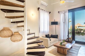 Una sala de estar moderna con una escalera, un sofá, una mesa de centro y vista a la playa.