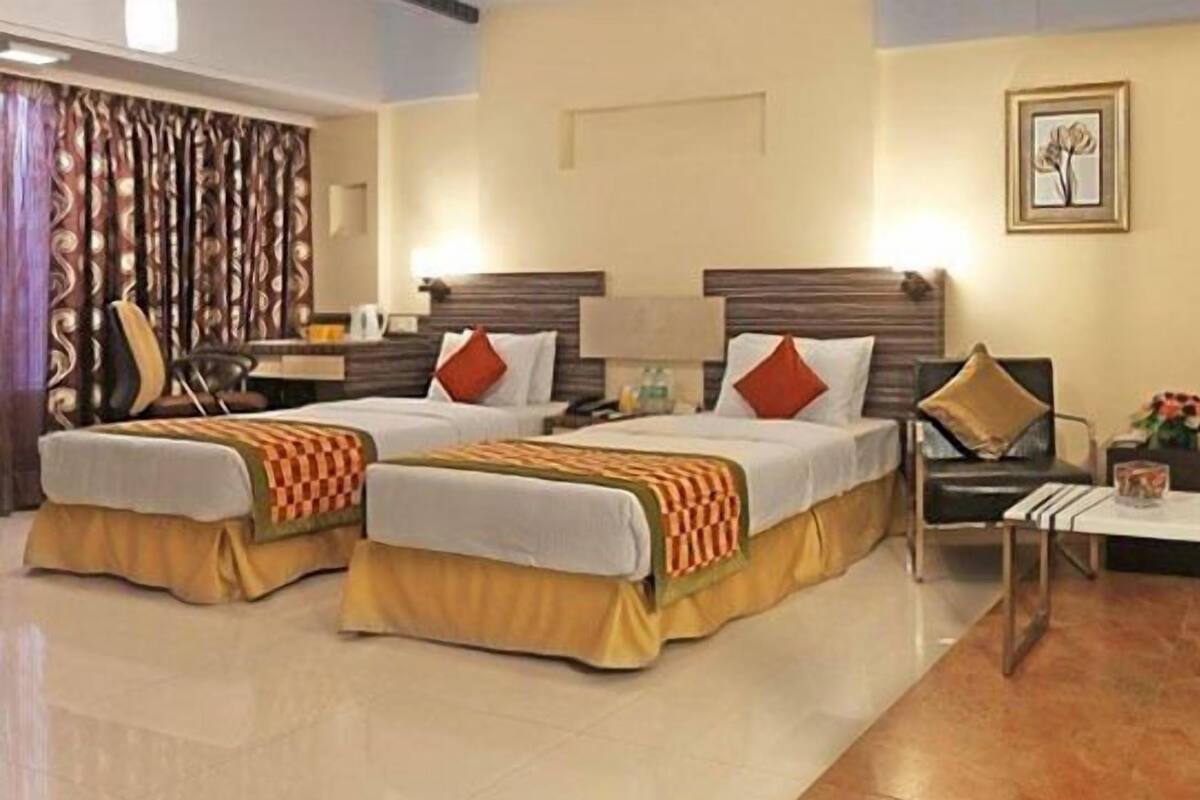Habitación de hotel con dos camas, una mesita, una silla y un panel decorativo en la pared.
