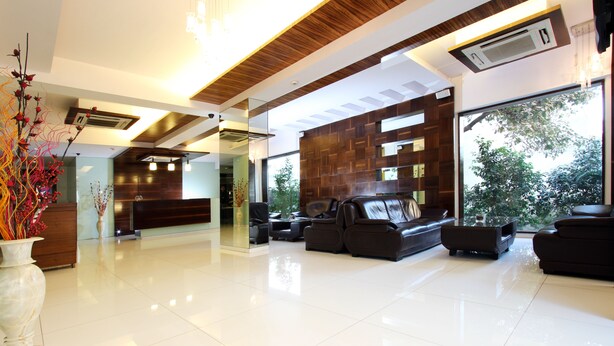 A modern reception area with a wooden reception desk, leather seating, and large windows offering a view of greenery. - Keys Select by Lemon Tree Hotels, Nestor, Mumbai (Mumbai)