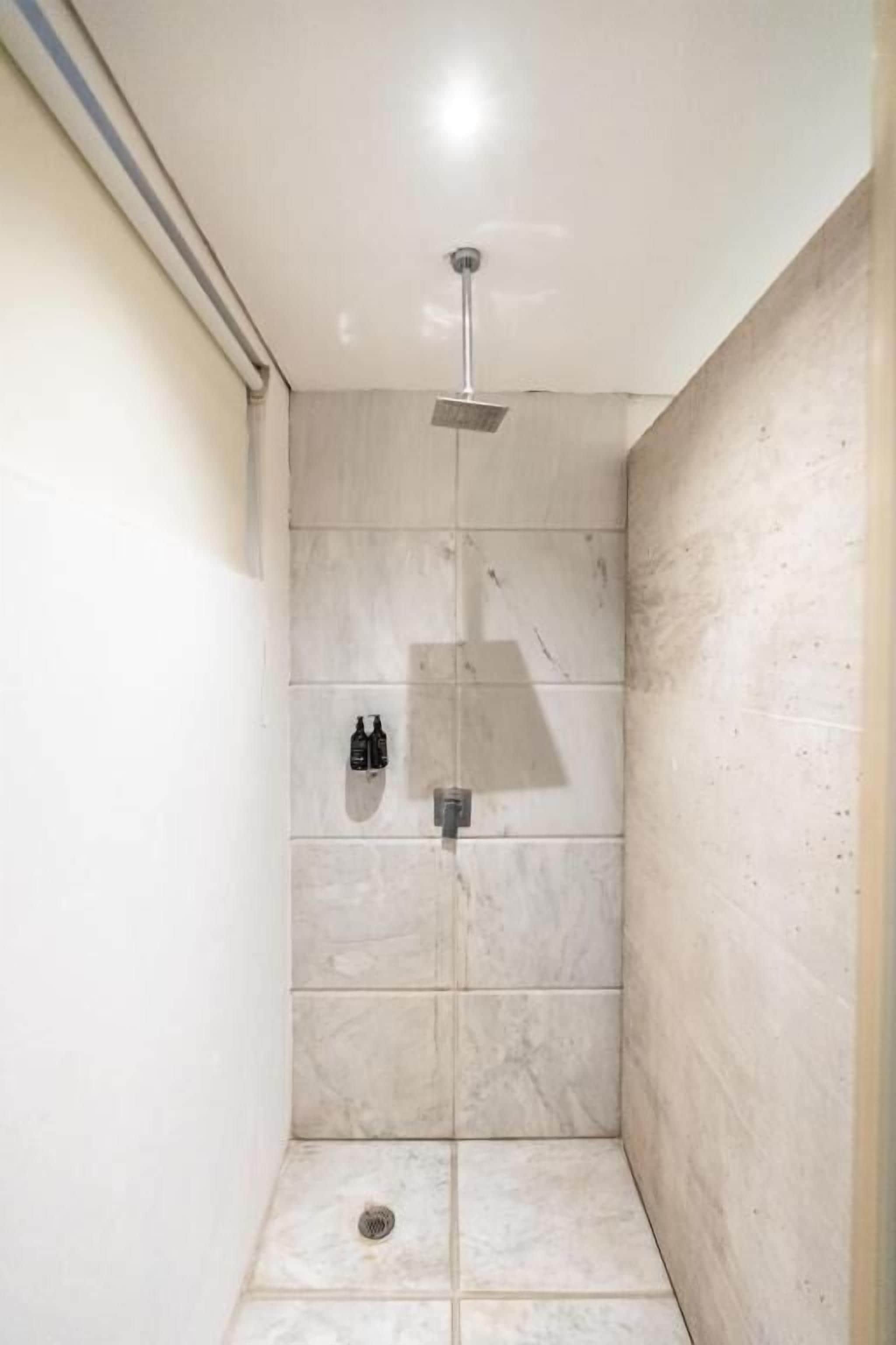 A shower with a handheld showerhead, a wall-mounted control panel, and a tiled floor.