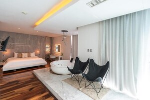 Un dormitorio moderno con una cama grande, una zona de estar con sillas, una bañera y un tocador con espejo.