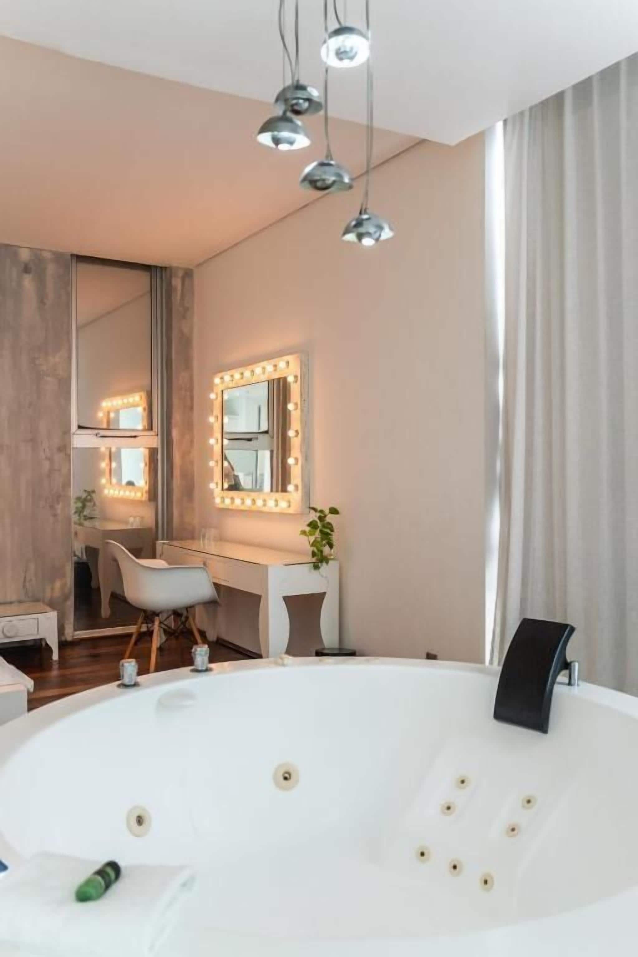 A modern bathroom with a large bathtub, vanity with a mirror, and pendant lighting.