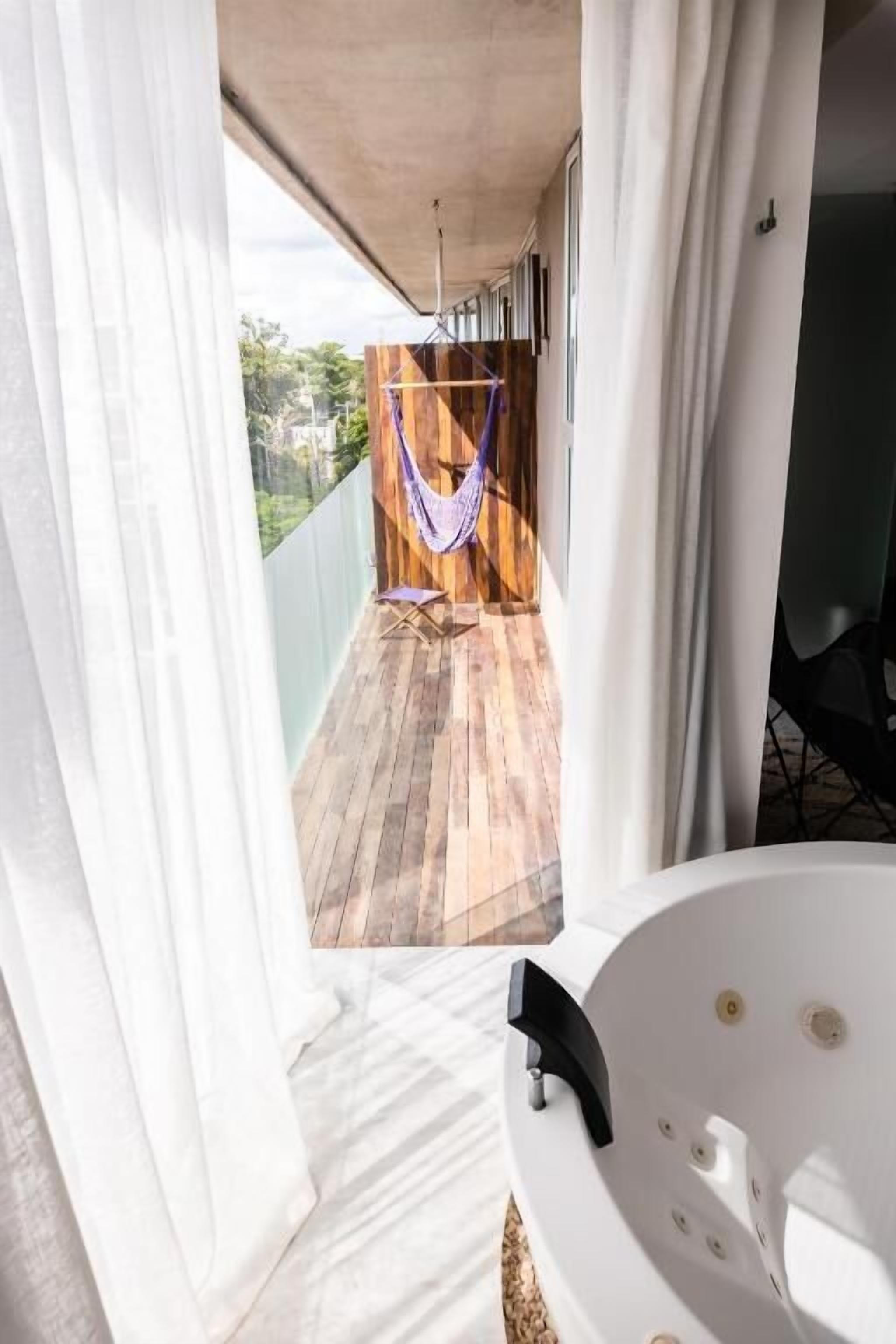 En balkon med hængekøje, trægulv og et hvidt badekar.
