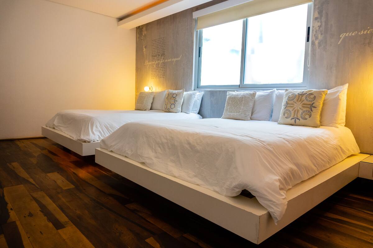 Un dormitorio moderno con dos camas, un ventanal grande y suelo de madera.