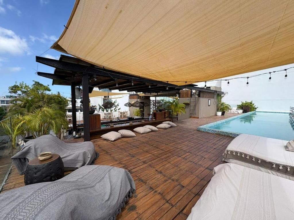 A rooftop terrace with a pool, lounge chairs, and a covered seating area.