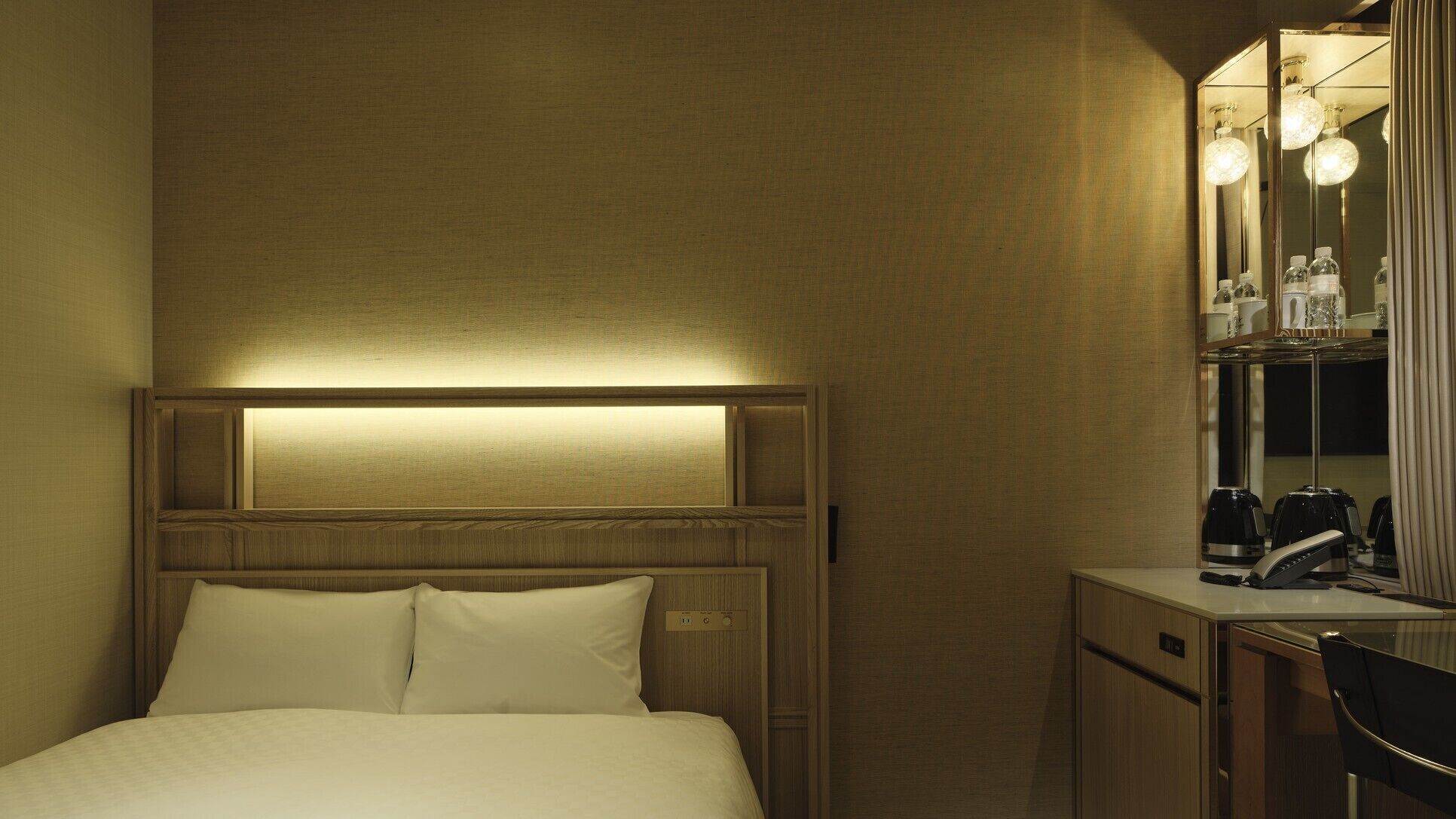 Una habitación de hotel con cama, mesita de noche y espejo con iluminación.