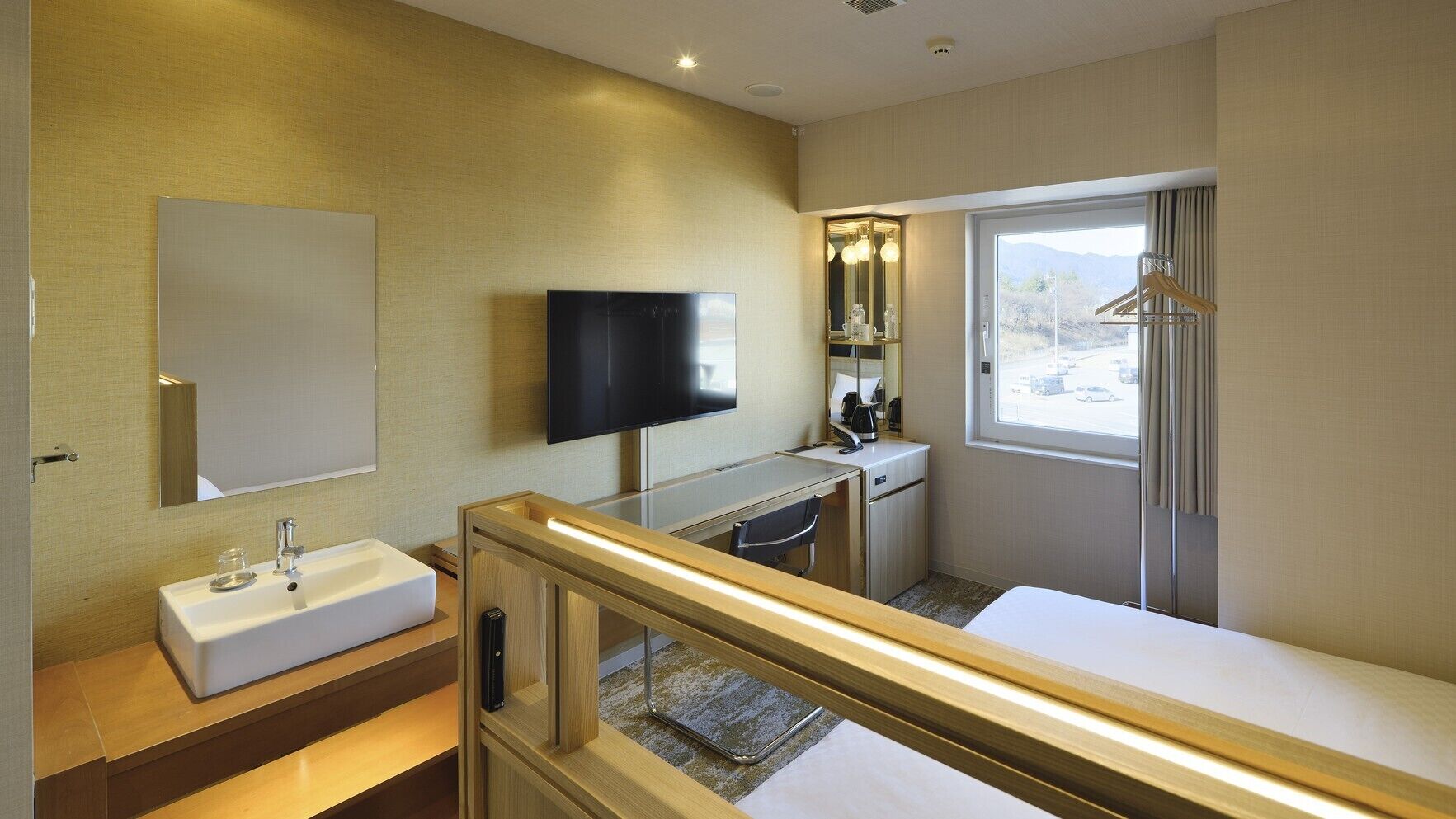 Une chambre d’hôtel équipée d’un lit, d’un bureau, d’une télévision, d’un miroir et d’une fenêtre donnant sur un paysage agréable.
