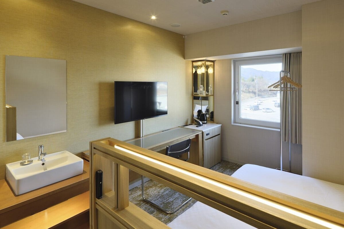 A hotel room with a bed, a desk, a TV, a mirror, and a window with a view.