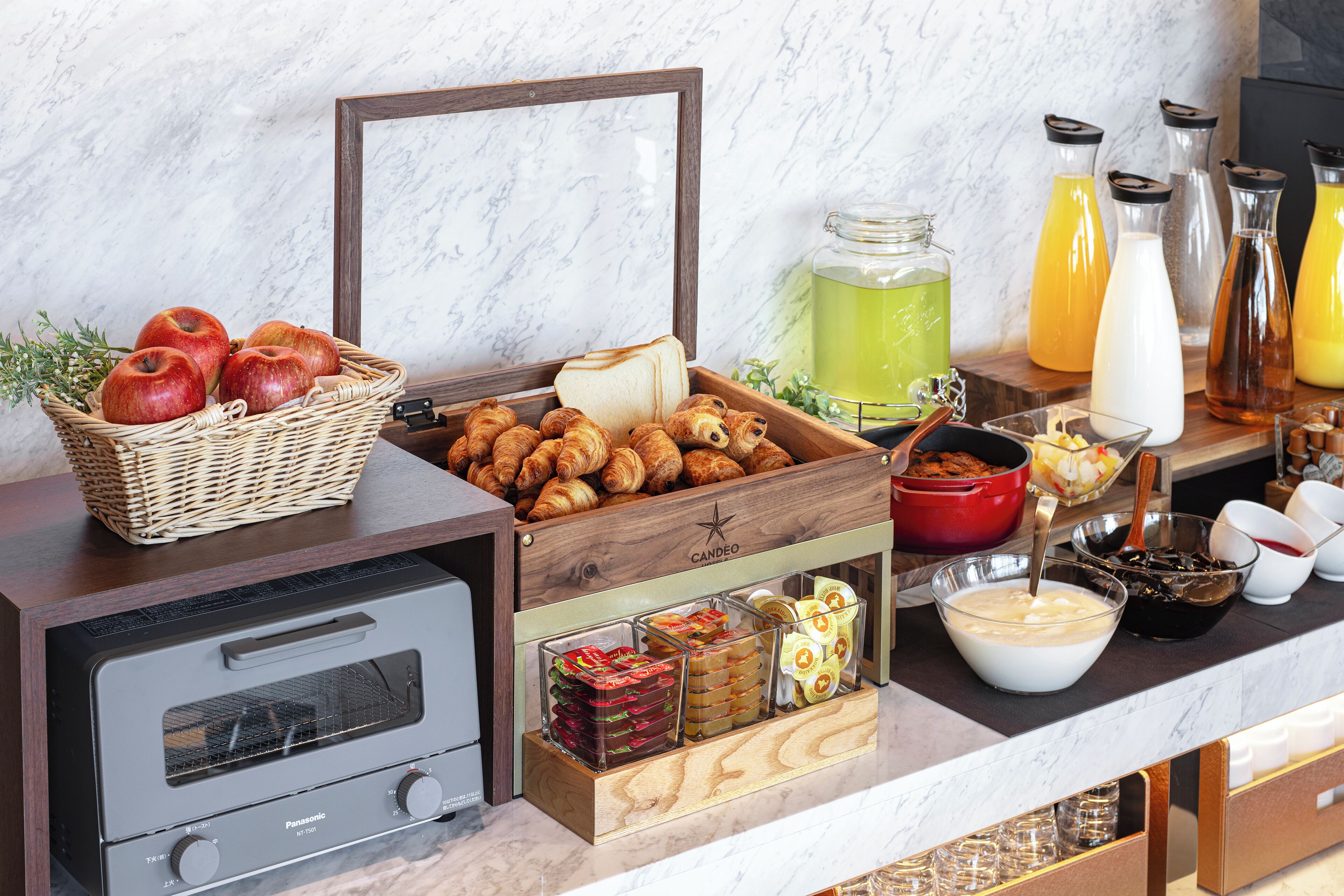 Un bufé de desayuno con diferentes alimentos, un tostador y dispensadores de bebidas.