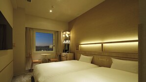 Quarto de hotel com uma cama grande, uma escrivaninha, uma cadeira, um espelho e uma janela com vista para a cidade.