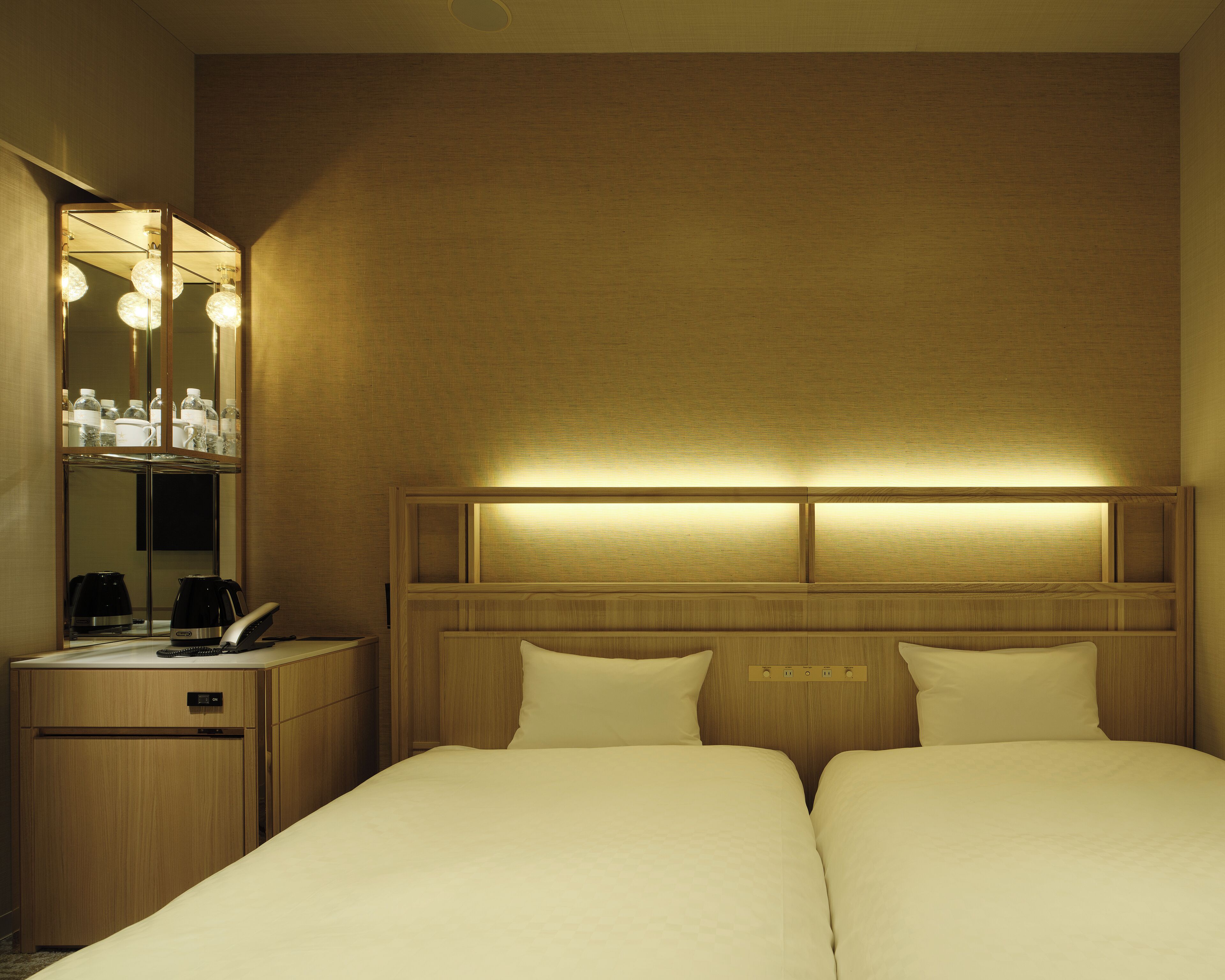A hotel room with a bed, bedside tables, a mirror, and a headboard with built-in lighting.