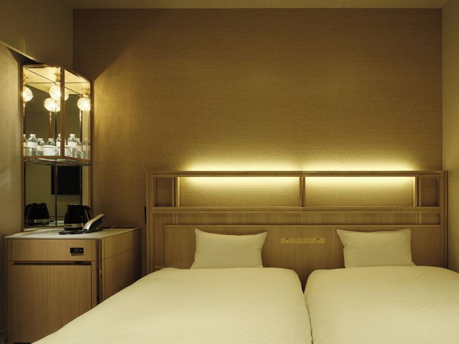 A hotel room with a bed, bedside tables, a mirror, and a headboard with built-in lighting.