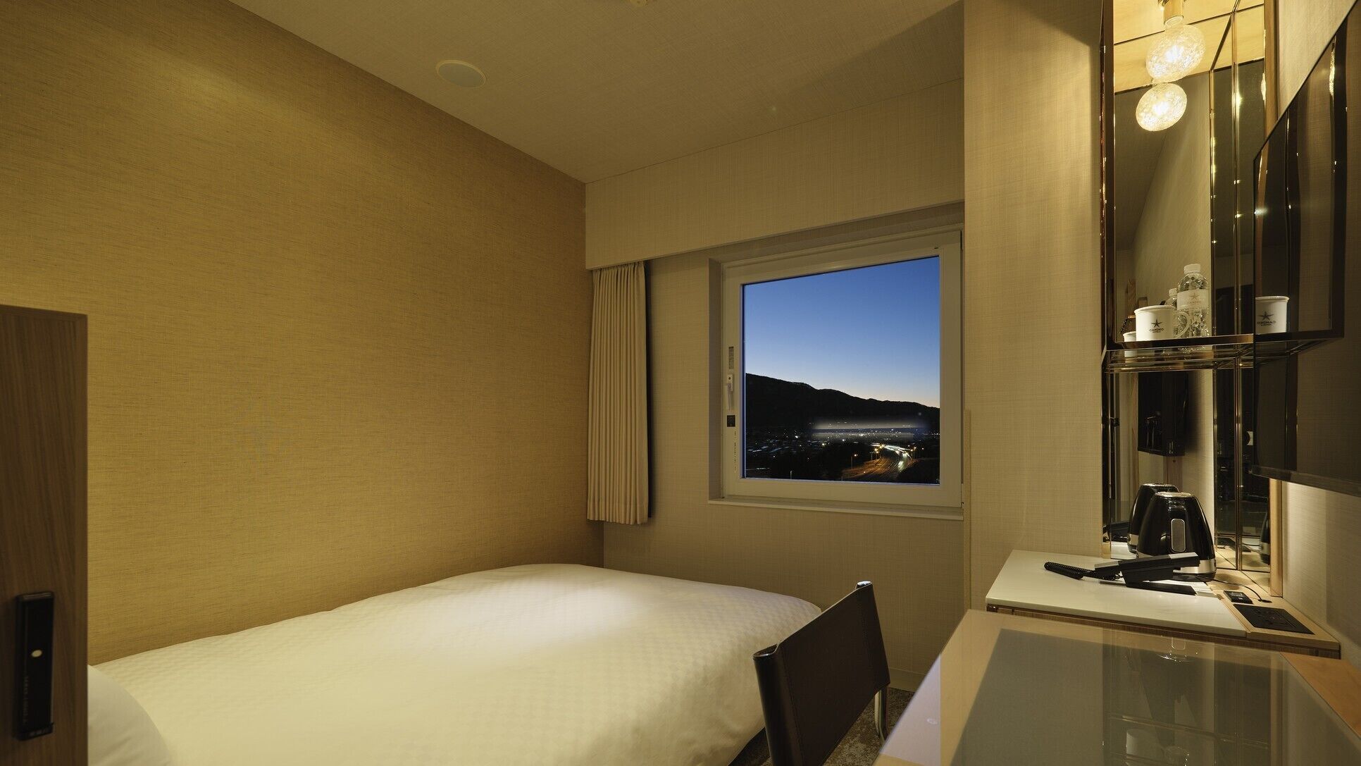 Une chambre d’hôtel avec un lit, un bureau équipé d’un ordinateur, une fenêtre donnant sur un paysage et un miroir.