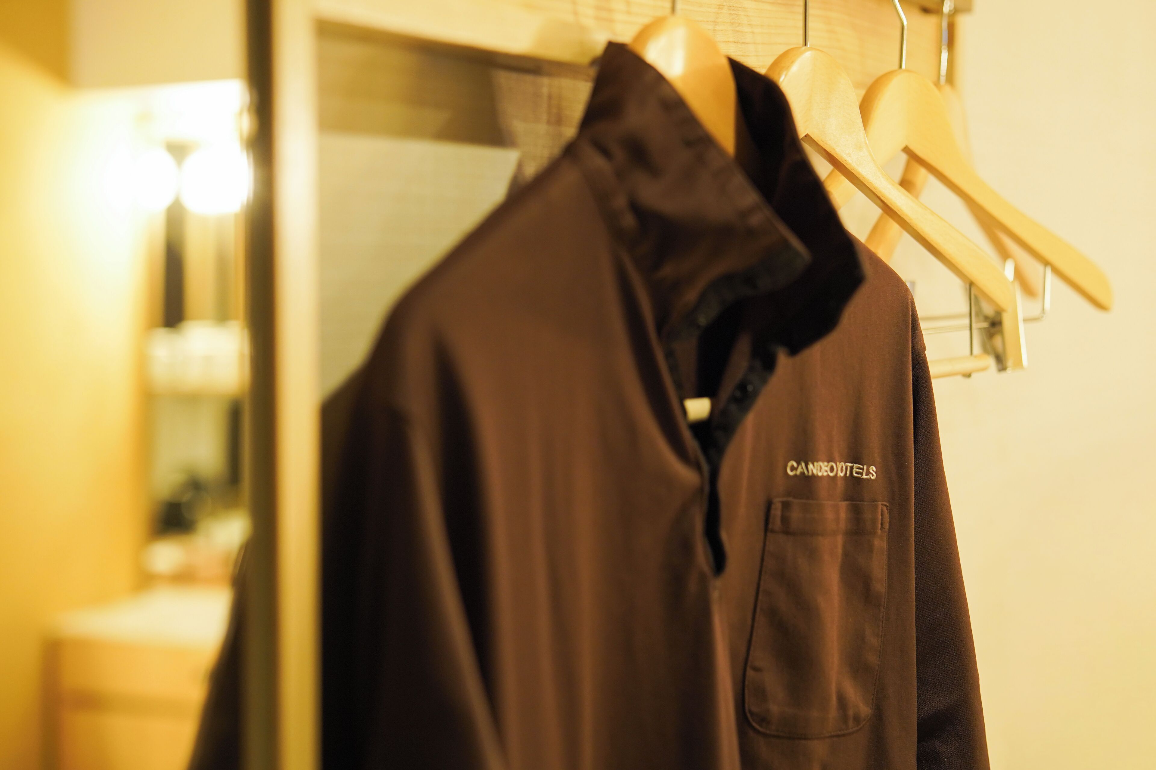 Une veste marron est suspendue à un cintre en bois, et on peut voir une poche ainsi qu’une étiquette sur laquelle est inscrit « CANDLE O’NEALS ».
