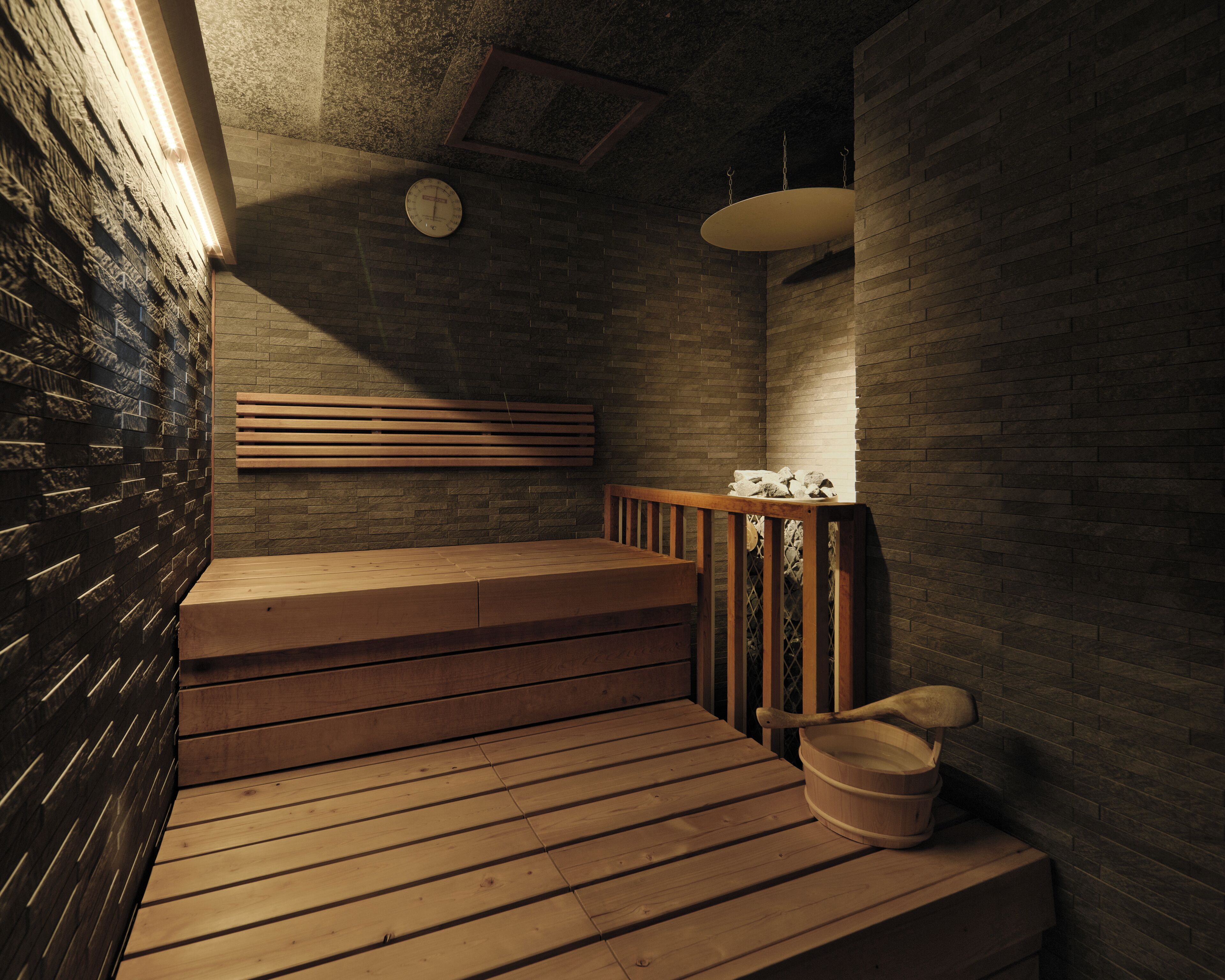 A sauna with wooden benches, a wooden bucket, and a wall clock.