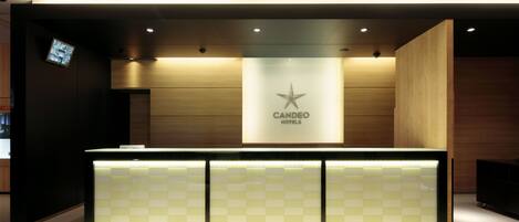 A reception desk with a checkered pattern, a star logo, and the text "CANDEO HOTELS" on the wall behind it.