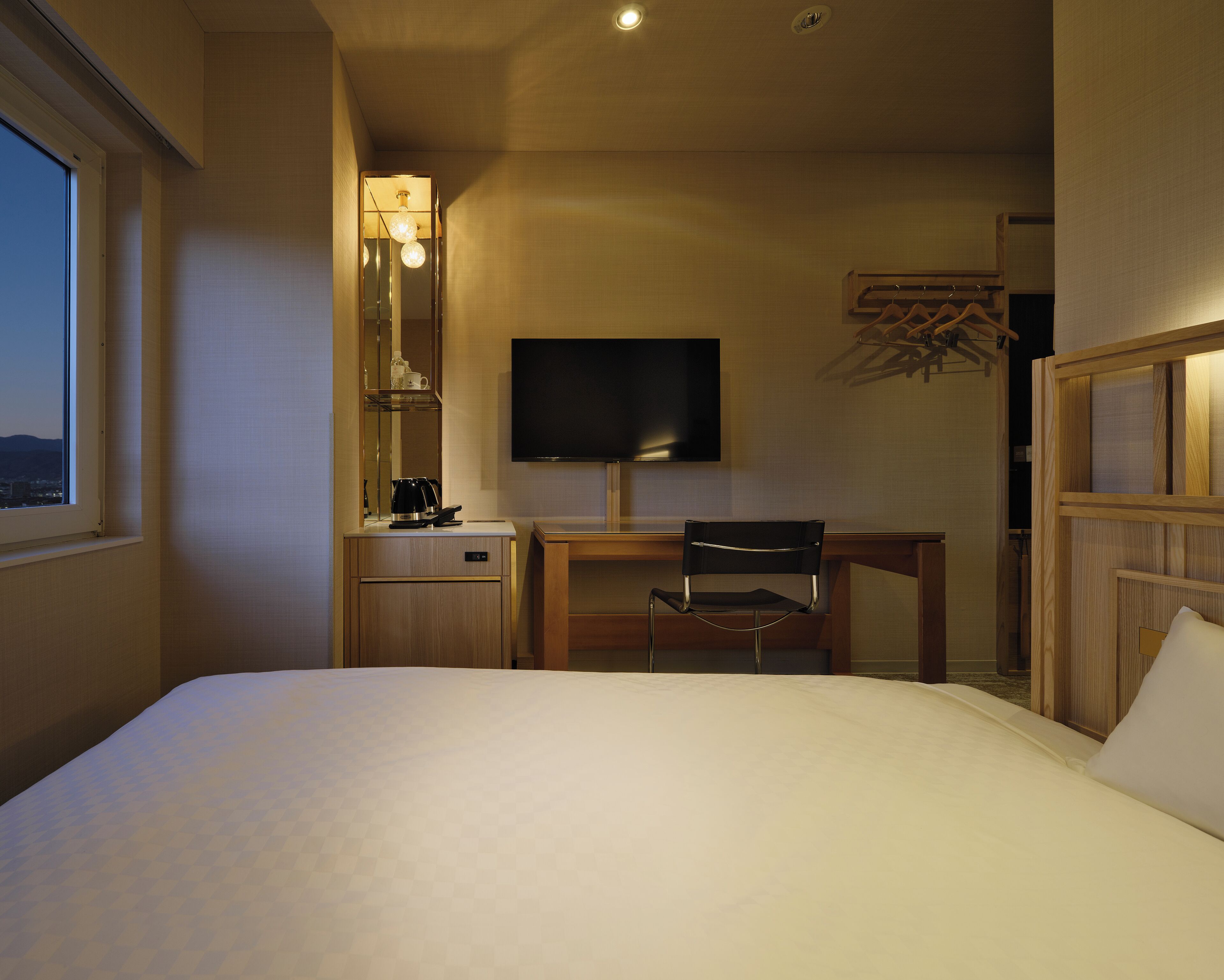 A hotel room with a bed, a desk, a chair, a television, and a window.