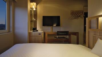 A hotel room with a bed, a desk, a chair, a television, and a window.