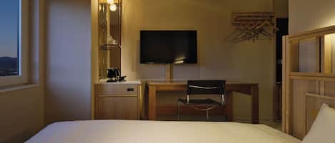 A hotel room with a bed, a desk, a chair, a television, and a window.