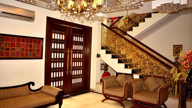 A grand staircase with ornate gold railings and a chandelier, leading to a second floor. - Rajputana Haveli (Jaipur)