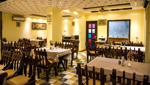 A dining area with multiple tables and chairs, a patterned ceiling, and a television screen on the wall. - Rajputana Haveli (Jaipur)