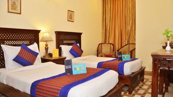 A hotel room with two beds, each with a blue and red striped bedspread, a wooden headboard, a nightstand with a lamp, and a small table with a vase of flowers.