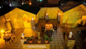 A rooftop patio with a tiled floor, outdoor seating, potted plants, and lanterns. - Rajputana Haveli (Jaipur)