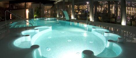 Una piscina interior de diseño circular, con varios jacuzzis y vistas a la ciudad a través de amplios ventanales.
